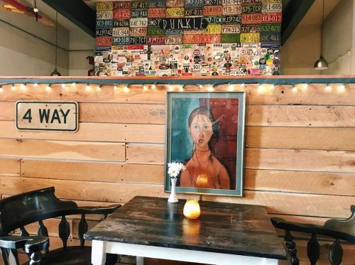 Cozy café interior with wooden walls, a framed painting, a small table with a candle, and a vintage sign.