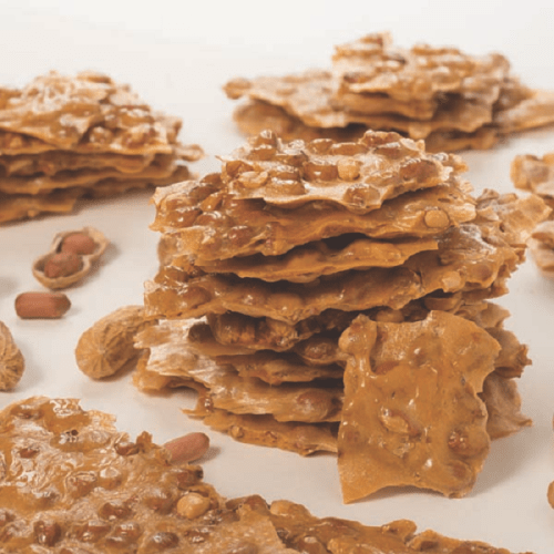 A stack of crunchy peanut brittle pieces scattered on a white surface.