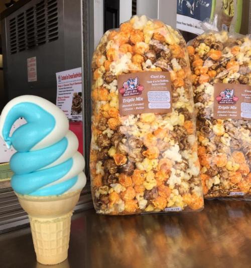 A soft-serve ice cream cone with blue and white swirls next to a bag of colorful popcorn mix.