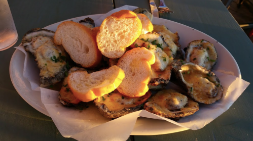 A plate of baked oysters topped with cheese, garnished with parsley, and served with slices of toasted bread.