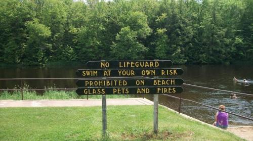 Sign by a river warning: "No lifeguard, swim at your own risk. Prohibited on beach: glass, pets, and fires."