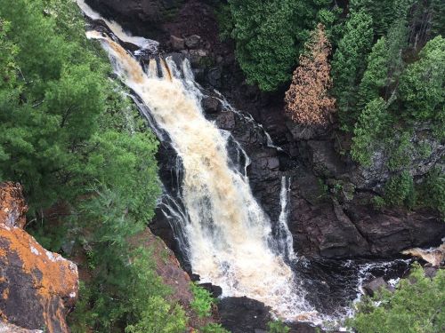 A cascading waterfall flows through rocky terrain, surrounded by lush green trees and a hint of autumn colors.