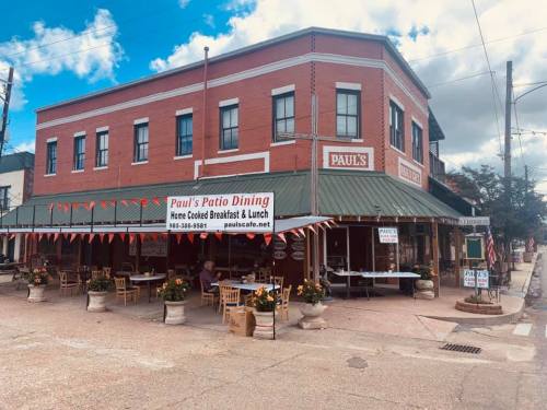 A red brick restaurant with outdoor seating, featuring a sign for "Paul's Patio Dining" and festive decorations.