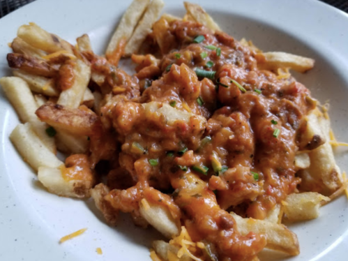 A plate of French fries topped with a cheesy, meaty sauce and sprinkled with green onions.