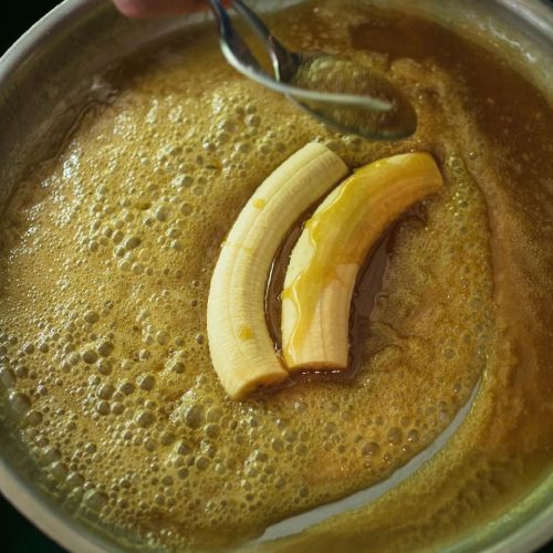 Sliced bananas simmering in a bubbling caramel sauce in a metal pan.