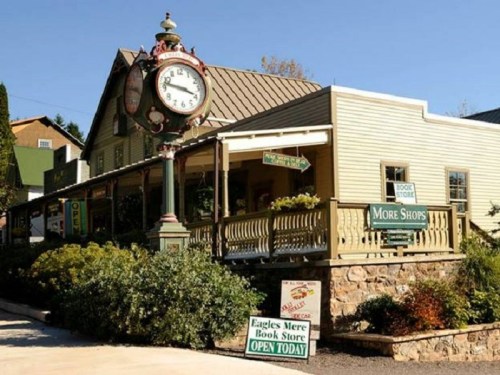 A charming storefront with a vintage clock, featuring signs for a bookstore and other shops in a quaint setting.