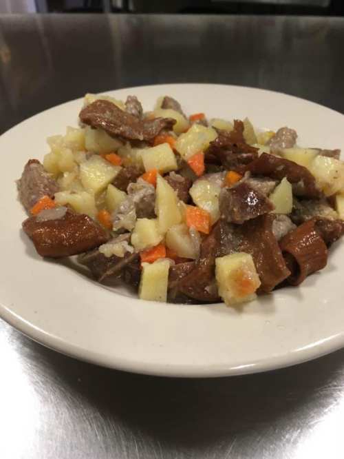 A plate of mixed vegetables and meat, including potatoes, carrots, and pieces of cooked meat, served on a white dish.