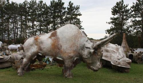 A large, weathered sculpture of a bull stands in a grassy area, surrounded by other abstract sculptures and trees.
