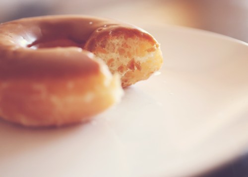 A glazed donut on a white plate with a bite taken out of it.