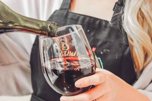 A person in an apron pours red wine into a glass, capturing a moment of wine tasting or serving.