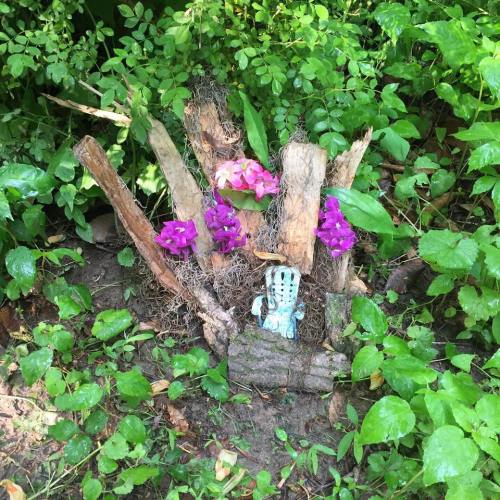 A small, whimsical sculpture surrounded by purple flowers and greenery in a lush garden setting.