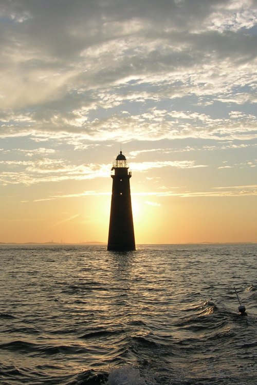 A silhouette of a lighthouse against a sunset, with waves gently rippling in the foreground.