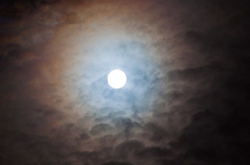 A bright sun partially obscured by swirling, colorful clouds in a dramatic sky.