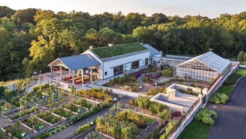 Aerial view of a modern building with a green roof, surrounded by lush gardens and a greenhouse.