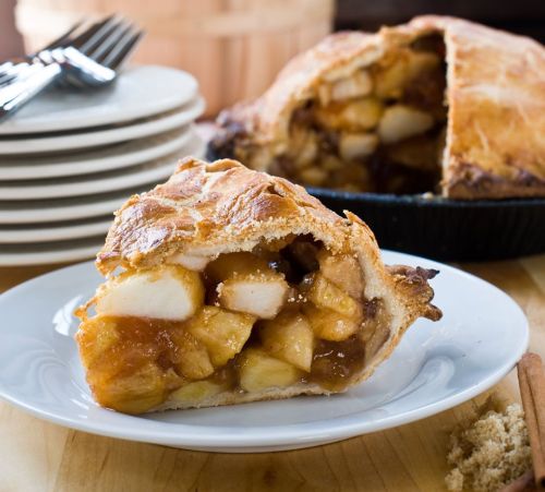 A slice of apple pie on a plate, showcasing a golden crust and a filling of apples and caramel.