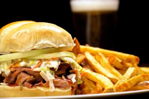 A close-up of a sandwich with roast beef, lettuce, and mayonnaise, served with a side of golden fries and a blurred drink in the background.