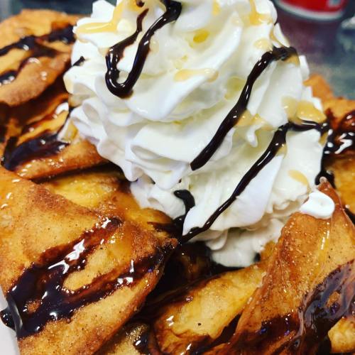 A plate of crispy dessert nachos topped with whipped cream, chocolate drizzle, and caramel sauce.