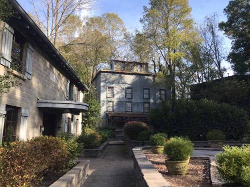 A serene garden scene featuring a gray building surrounded by trees and landscaped greenery.