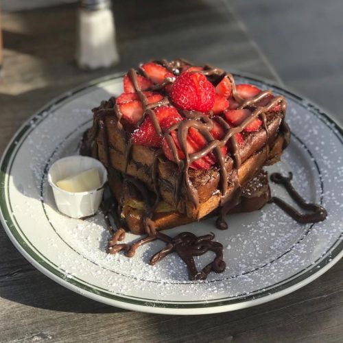 A plate of decadent French toast topped with strawberries and drizzled with chocolate sauce, served with a side of cream.