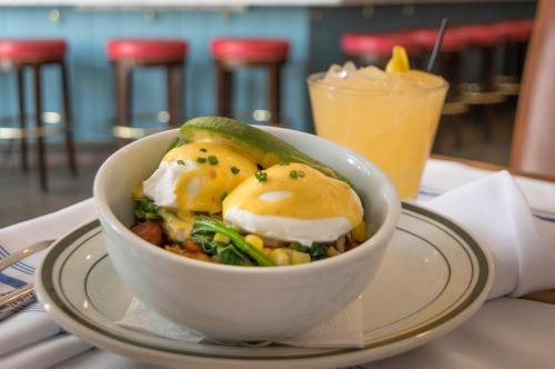 A bowl of eggs Benedict with spinach and hollandaise sauce, served with a cocktail in the background.