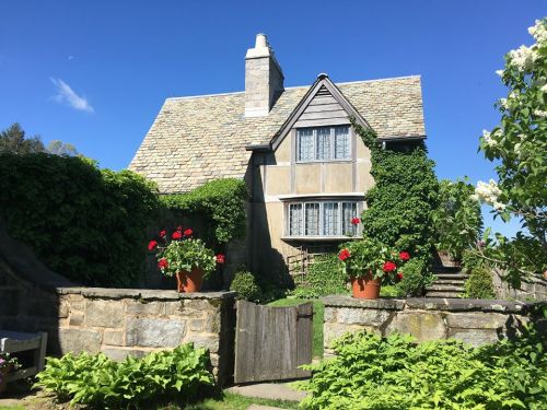 A charming stone house surrounded by greenery and flowers, under a clear blue sky.