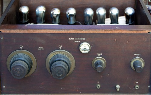 Vintage radio equipment with knobs for volume and tuning, featuring glass vacuum tubes and a wooden casing.