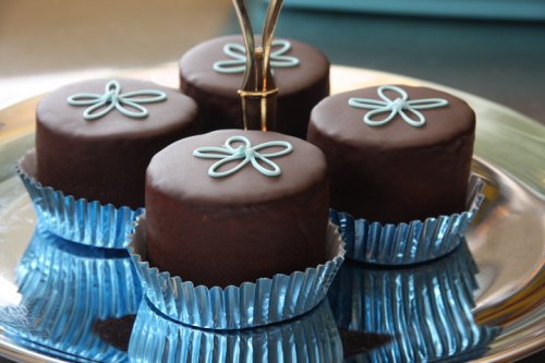 Four chocolate-covered cakes with blue flower designs on top, arranged on a shiny silver platter.