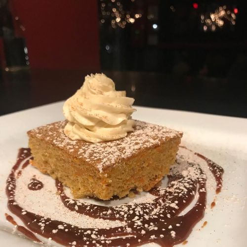 A slice of cake topped with whipped cream, dusted with powdered sugar, on a plate with chocolate sauce swirls.