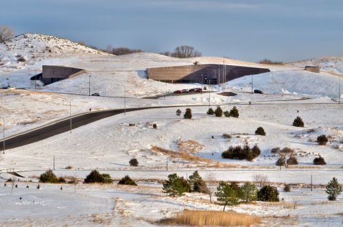A modern building set against a snowy landscape, with a winding road and sparse trees in the foreground.