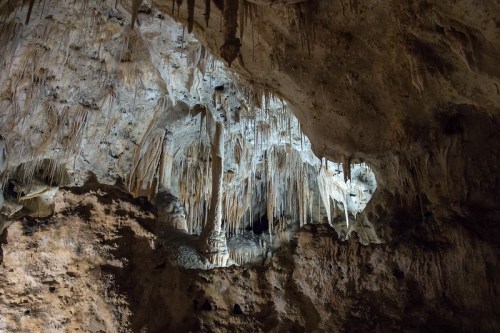 Stalactites and stalagmites in a dimly lit cave, showcasing intricate rock formations and textures.