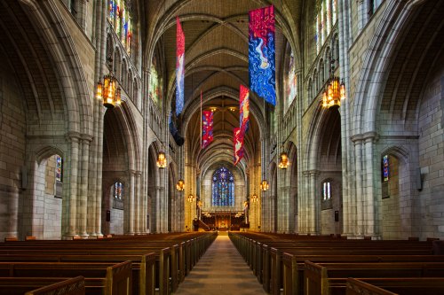 Interior of a grand church featuring tall arches, wooden pews, colorful banners, and stained glass windows.