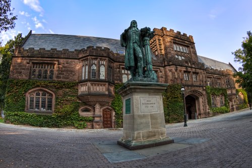 Statue of John Witherspoon in front of a historic ivy-covered building under a clear blue sky.
