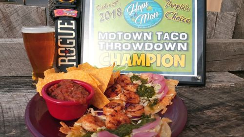 A plate of tacos with shrimp, salsa, and tortilla chips, alongside a beer and a "Champion" award sign.