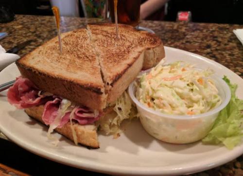 A toasted sandwich filled with meat and coleslaw, served with a side of creamy coleslaw in a small bowl.