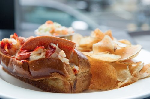 A lobster roll filled with lobster meat, served with a side of crispy potato chips.