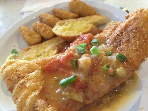 A plate featuring a seasoned fish fillet topped with a tomato sauce, accompanied by golden fried potatoes and toast.