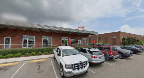 Exterior view of a brick building with a sign reading "Frey," featuring parked cars and a cloudy sky.