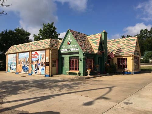 Colorful building with a mural, featuring a green and tan exterior, and a sloped, multicolored roof.