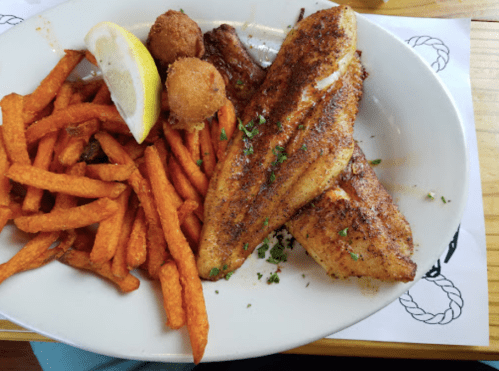 A plate with two seasoned fish fillets, sweet potato fries, a lemon wedge, and two hushpuppies.