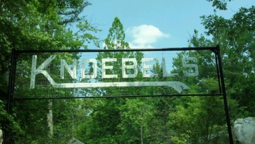 Sign for Knoebels amusement park surrounded by lush green trees and a blue sky.