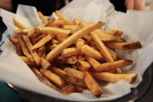 A basket filled with golden, crispy French fries on a bed of white paper.