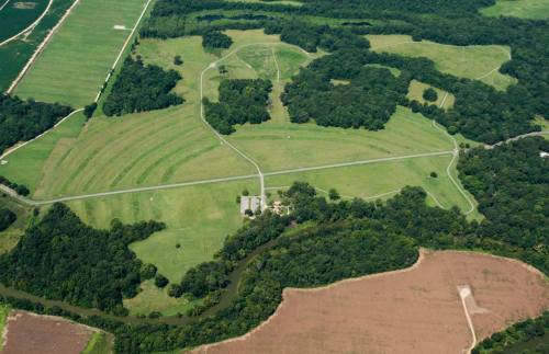 Aerial view of a large, green landscape with winding roads, fields, and a river running through the area.