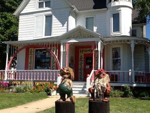 A charming white house with pink accents, featuring two whimsical wooden sculptures in front.