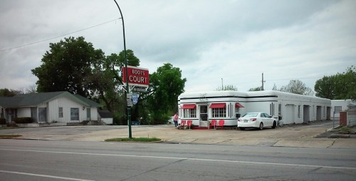 A retro diner-style building with red accents, next to a small house, under a cloudy sky.