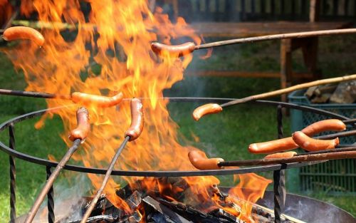 Sausages roasting over an open fire, with flames and smoke rising around them.