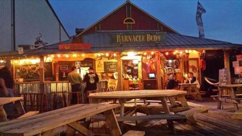 A cozy outdoor bar with wooden picnic tables, string lights, and a welcoming atmosphere at dusk.