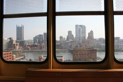 View of Pittsburgh skyline from a window, showcasing tall buildings and a river in the foreground.