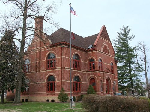 Historic red brick building with arched windows, a flagpole, and surrounding trees.