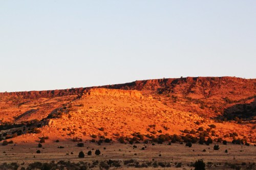 Sunset casts warm light on a rugged, rocky landscape with gentle hills and sparse vegetation.