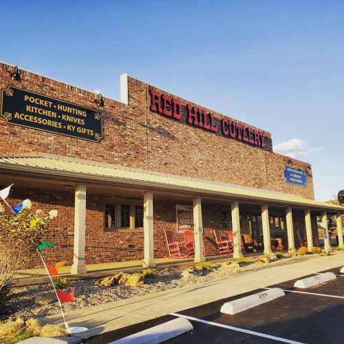 Exterior of Red Hill Cutlery store with brick facade, signs for various products, and a clear blue sky.